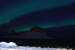 an aurora over a mountain in the snow at night at Sæból/Ocean Lair 2 in Grundarfjordur