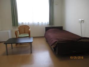 a bedroom with a bed and a chair and a table at Oyado Yamabiko in Ibusuki