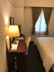 une chambre d'hôtel avec un lit et un bureau avec une lampe dans l'établissement Hotel Tsukuba Hills Umezono, à Tsukuba