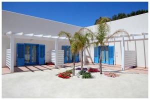 a white building with blue shuttered windows and palm trees at Plaia Case Vacanza in Favignana