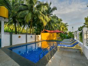 a swimming pool with two blue chairs and palm trees at OYO 15836 River Front Resort in Morjim