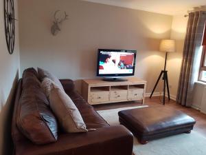 a living room with a brown leather couch and a television at Largs stay With Private parking in Largs