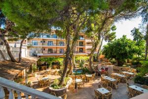 an outdoor restaurant with tables and chairs and trees at Hotel Baviera in Cala Ratjada