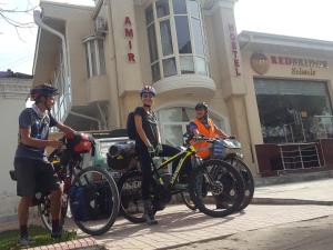 Tres hombres están parados con sus bicicletas delante de un edificio en Amir Hostel, en Samarkand