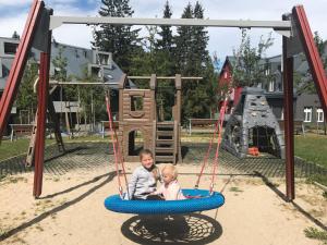 2 bambini seduti su un'altalena in un parco giochi di Resort 302 a Harrachov