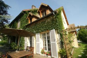 a house covered in ivy with a table and an umbrella at Le Cèdre Bleu in Grosrouvre