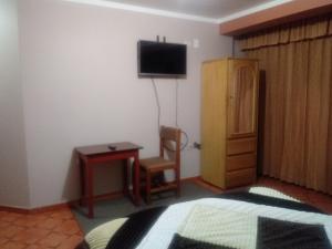 Habitación con TV, silla y mesa. en Hostal Intiwatana Inn, en Puno