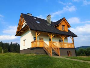 a house with a wrap around deck on a green field at Chata Wielki Potok in Istebna