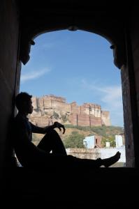 a man sitting in a window looking out at a mountain at The Arch Boutique Home stay in Jodhpur