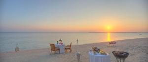 a table and chairs on the beach at sunset at The Residence Zanzibar in Kizimkazi