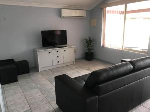 a living room with a black couch and a flat screen tv at Guesthouse on Dolphin in Safety Bay