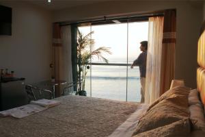a woman standing in a bedroom looking out the window at Hotel Riviera Muchik in Huanchaco