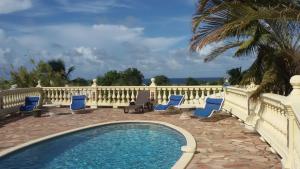 a swimming pool with blue chairs and a fence at LE MOULIN DE LA BAIE piscine vue mer in Le Moule