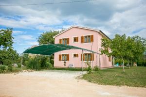 uma casa cor-de-rosa com um grande guarda-chuva verde em Pleasant Villa Valmonida with Pool, Sauna, Gym and BBQ em Žminj