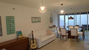 a living room with a couch and a table with a guitar at Pé na areia em Boiçucanga condominio Aquamarine - perto de Maresias e Camburi in Boicucanga