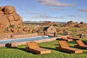 a pool with chairs and a building in the desert at Gondwana Canyon Village in Kanebis