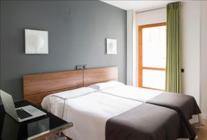een slaapkamer met een bed en een bureau met een laptop bij Hospedium Hostal Un Punto Chic in Huesca
