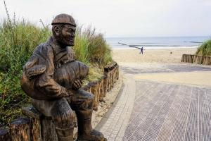 Una statua di un uomo seduto su una recinzione vicino alla spiaggia. di Schwab_ Ferienwohnungen in Zempin a Zempin