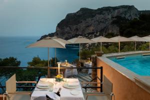 a dining table with umbrellas next to a swimming pool at Hotel Punta Tragara in Capri