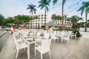 a restaurant with white tables and chairs and palm trees at HARRIS Resort Batam Waterfront in Sekupang