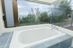 a bath tub in front of a window with a view at Akabana Inn in Nakijin