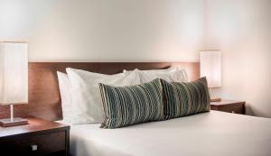 1 cama con almohadas blancas y 2 mesitas de noche con lámparas en Franklin Apartments, en Adelaida