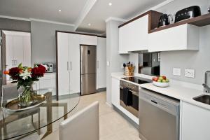 a kitchen with white cabinets and a glass table at SANDTON APARTMENT MASINGITA TOWERS 15 WEST Rd SOUTH in Johannesburg +7 photos