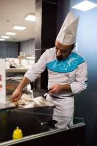 mężczyzna w kapeluszu kucharza przygotowujący jedzenie w kuchni w obiekcie Hotel Magnus Trenčín w Trenczynie