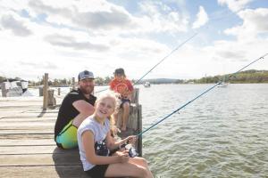 uma família sentada numa doca a pescar na água em BIG4 Karuah Jetty Holiday Park em Karuah