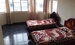 two beds sitting in a room with windows at Hostal Lesly Salome in Tulcán