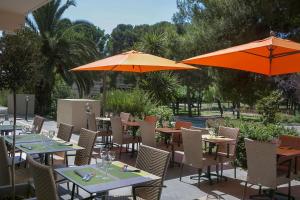 un patio avec des tables et des chaises et des parasols orange dans l'établissement Best Western Hôtel des Thermes - Balaruc les Bains Sète, à Balaruc-les-Bains