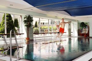 a man and a woman jumping in a swimming pool at Best Western Macrander Hotel Dresden in Dresden