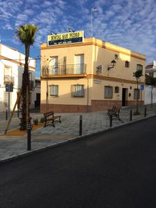 a building with two benches in front of a street at Hostal San Pedro in Sanlúcar la Mayor