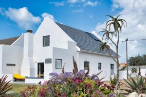 a white house with flowers in front of it at Amia House Struisbaai in Struisbaai