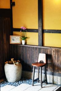 a stool and a vase next to a yellow wall at Guesthouse Mio in Omihachiman