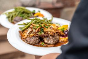 a person holding a plate of food with meat and vegetables at Frommanns Landhotel in Buchholz in der Nordheide