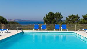 a swimming pool with four blue chairs and a fence at Duerming San Vicente Hotel in San Vicente do Mar