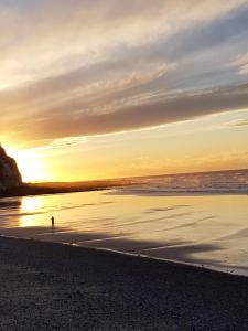 een persoon die bij zonsondergang op het strand staat bij Le Côte d'Albâtre in Tourville-la-Chapelle