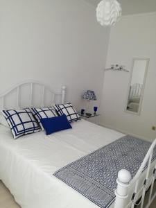een wit bed met blauwe kussens in een witte kamer bij Casa do Penedo in Vila Franca do Campo