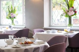 a dining room with two tables with white tableclothsurrencyangering at Antoinette Hotel Wimbledon in London