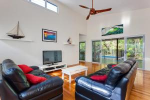 a living room with two leather couches and a tv at Sandyfeet House in Rainbow Beach
