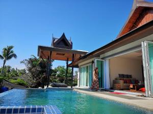 a woman standing next to a swimming pool next to a house at JJ Queen Villa and Spa Kohyaonoi in Ko Yao Noi