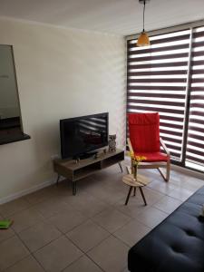 ein Wohnzimmer mit einem TV und einem roten Stuhl in der Unterkunft Depto Piso 4 Altos del Brillador in La Serena