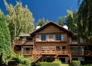 duży drewniany dom z drzewami przed nim w obiekcie Pailahue Cabañas Lodge w mieście Bariloche