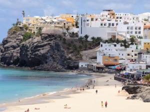 a group of people on a beach with buildings at Calle Buenavista 1, esquina boulevar Timón. in Morro del Jable