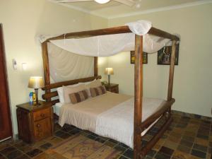 ein Schlafzimmer mit einem hölzernen Himmelbett mit weißer Bettwäsche in der Unterkunft Trees Too Guest Lodge in Komatipoort