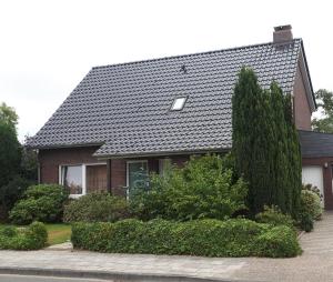uma casa com um telhado preto e alguns arbustos em Ferienwohnung Gesine em Leer