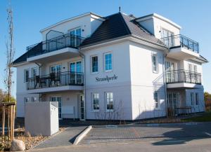 a white building with a black roof at Fewo Strandleben Haus Strandperle in Börgerende-Rethwisch