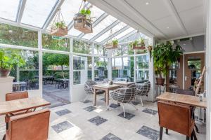 einen Wintergarten mit Tischen, Stühlen und Fenstern in der Unterkunft Hajé Restaurant de Aalscholver in Lelystad