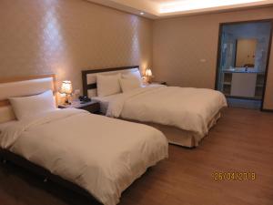 two beds in a hotel room with white sheets at Mao Hua Motel in Dajia